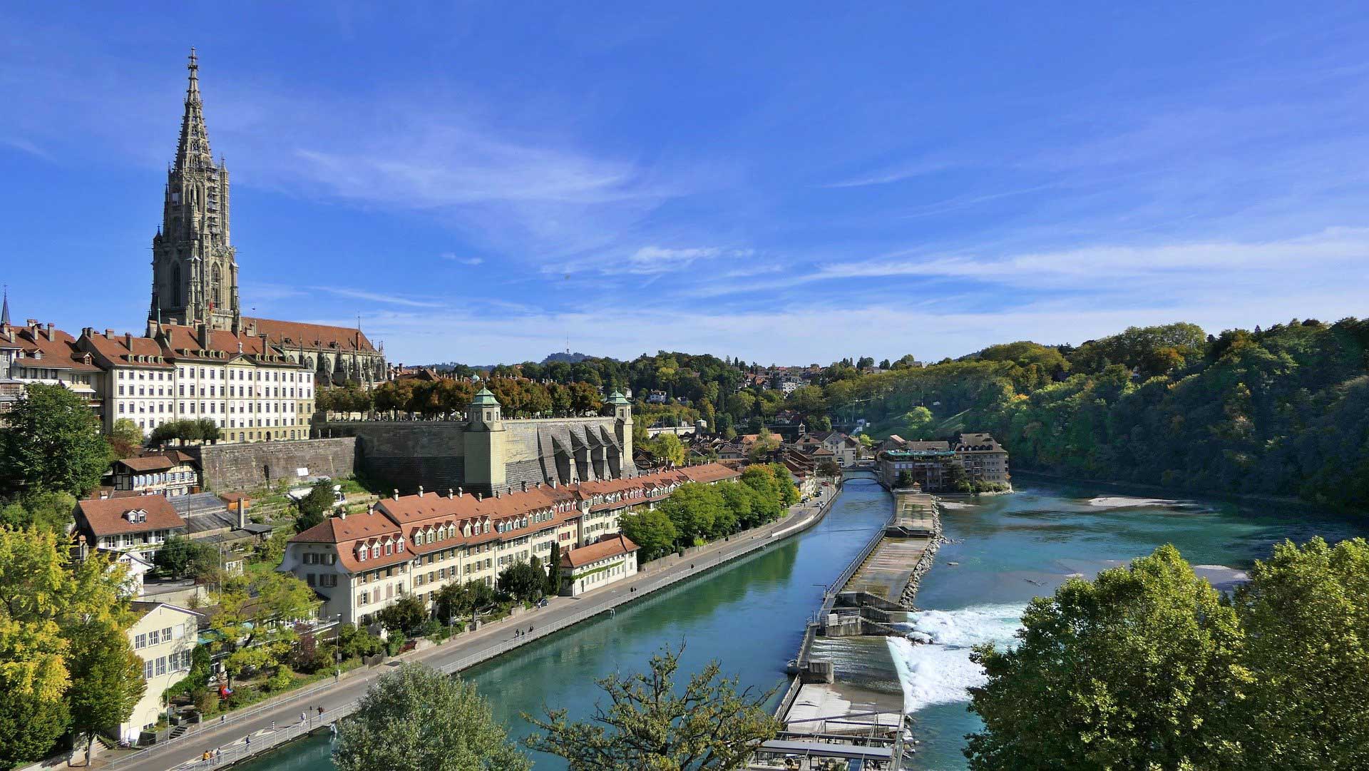 Cathedral overlooking a beautiful river in bern switzerland clear blue skies with buildings along the river around the world top 5