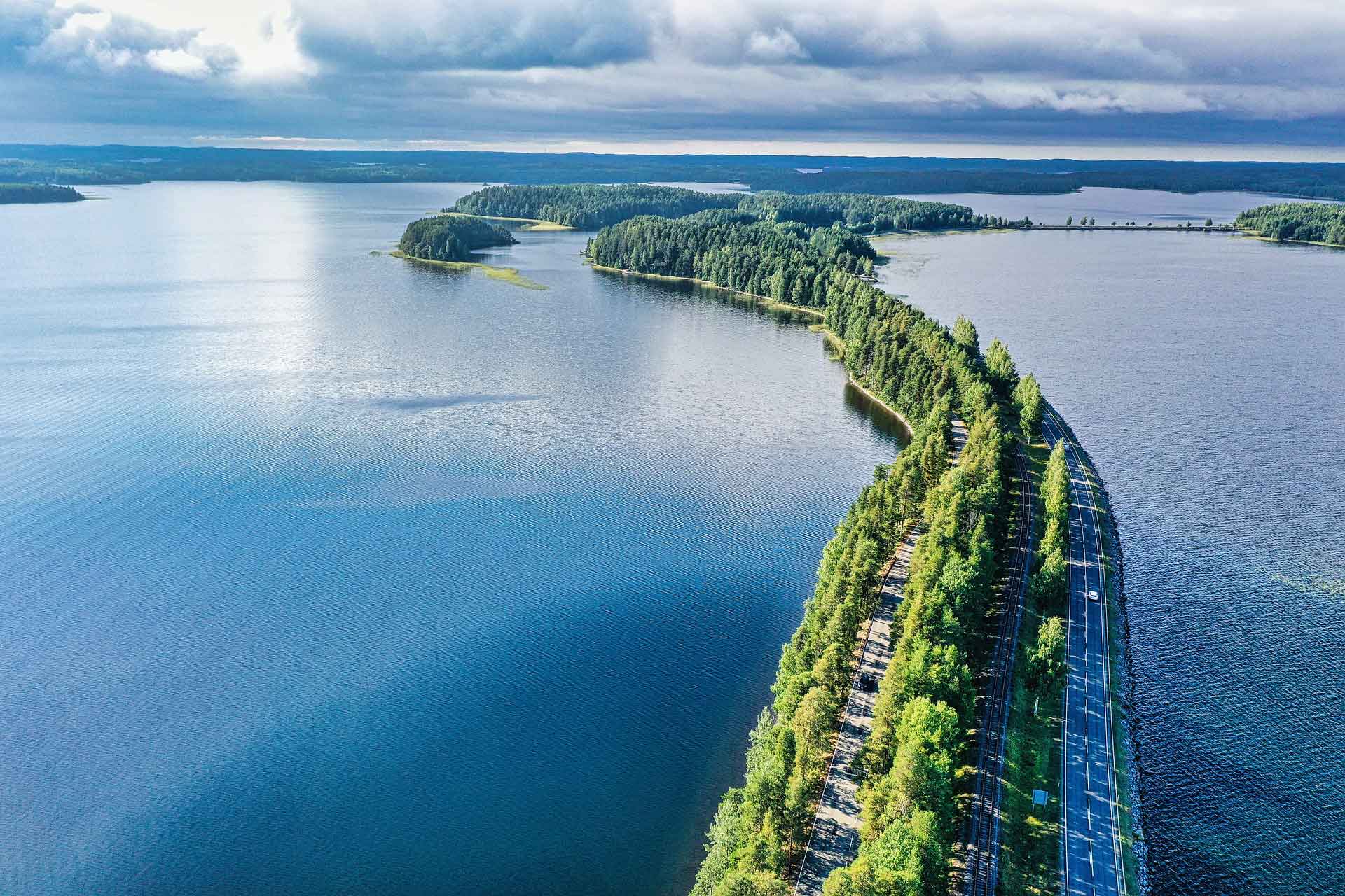 Narrow ridge of trees in the middle of big body of water in finland around the world top 5 blue cloudy skies with blue waters below