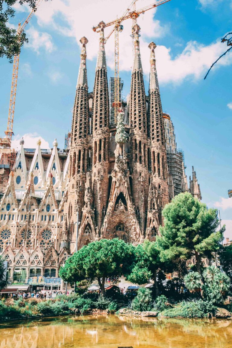 Large cathedral called la sagrada familia in barcenlona, trees in front of church and clear blue skies