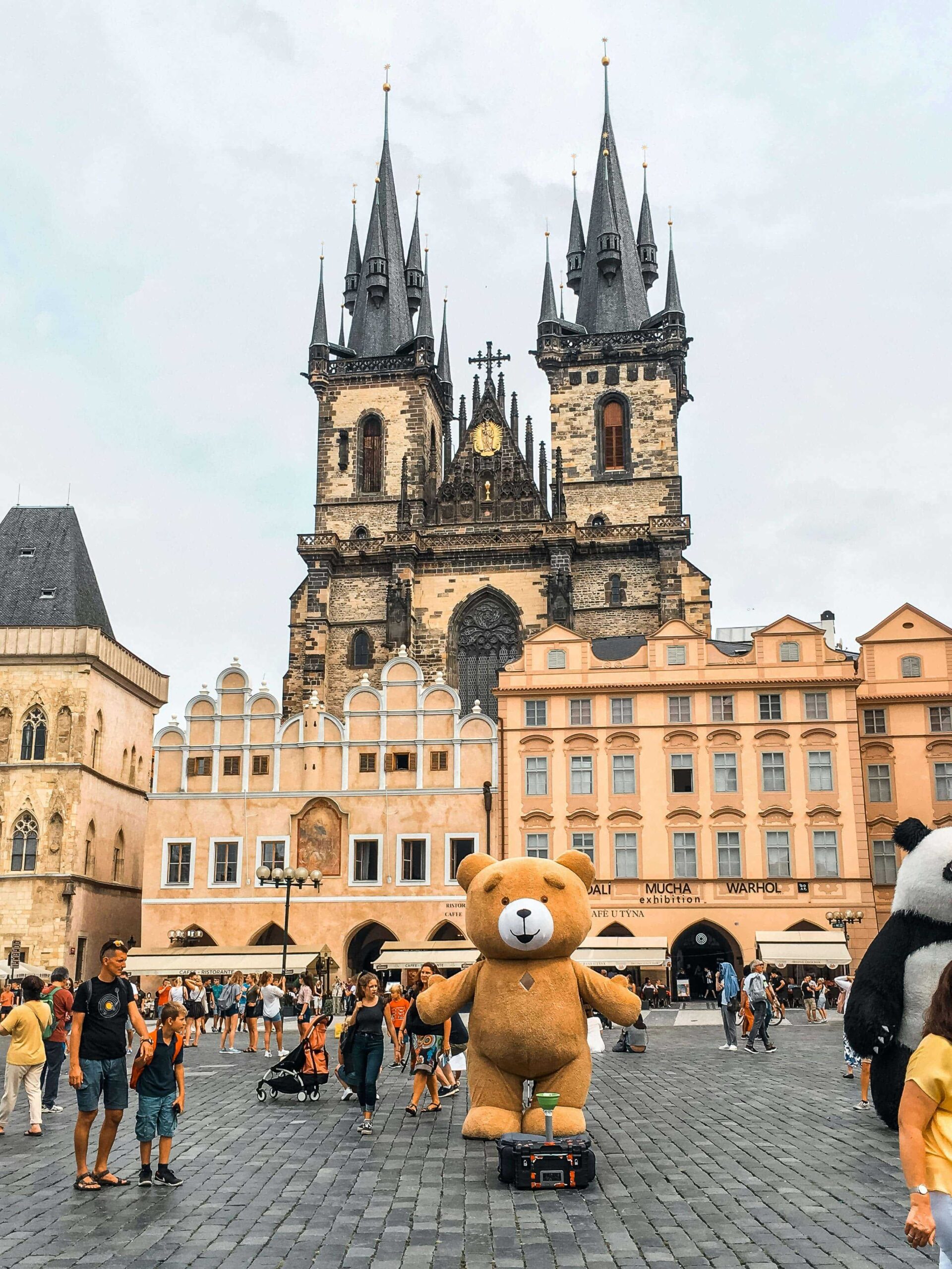 big teddy bear in the center of the square in the city of prague some people in the crowd with a large cathedral building in background