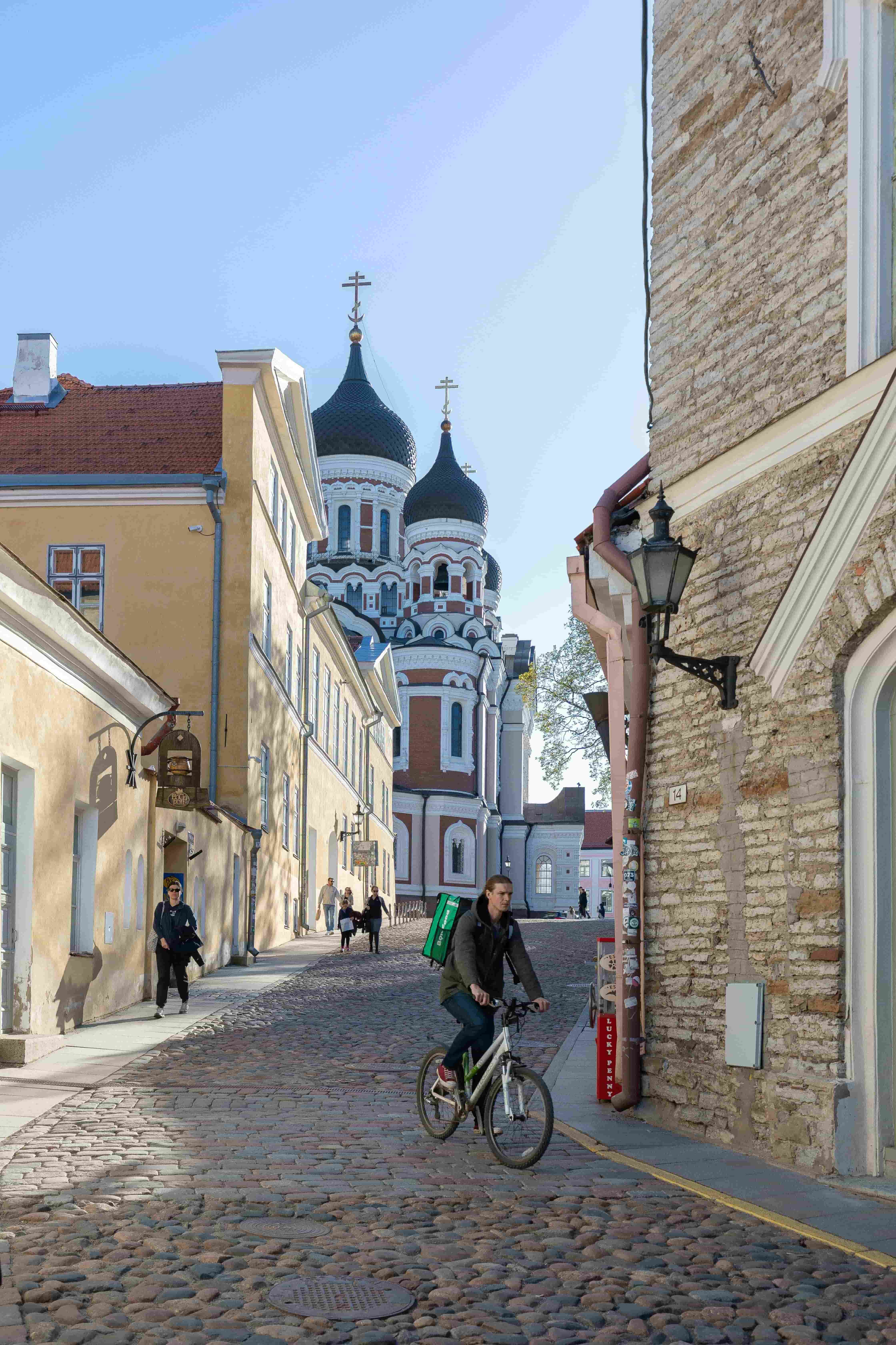 narrow streets of tallinn estonia with man riding bike clear blue skies