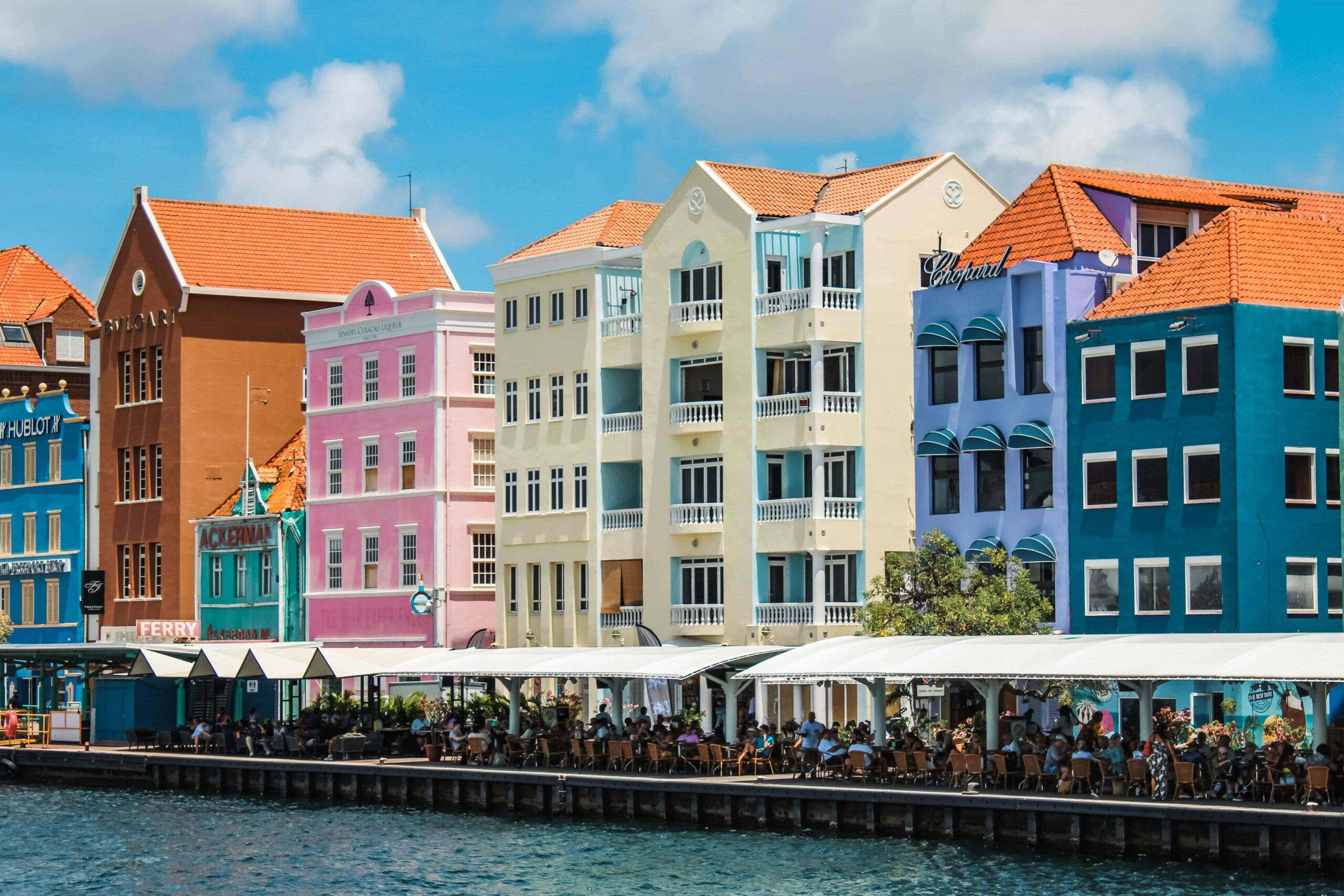 beautiful colorful buildings along the water in curacao the buildings are orange, pink, yellow, blue, green, with blue clear skies.