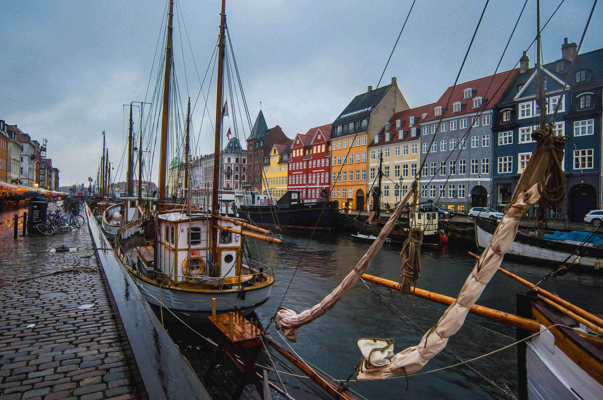 copenhagen harbor with a sail ship in the canal and buildings along the edge, clear blue skies in denmark